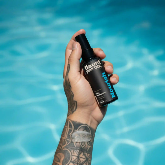 Hand holding a bottle of ' flaunt your INK' daily moisturiser nourish with a pool in the background