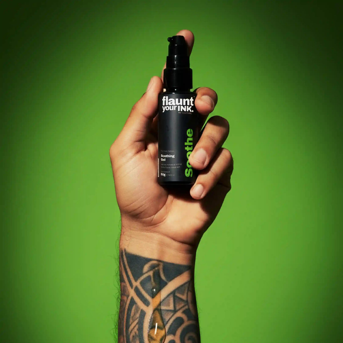 Hand holding a bottle of ' flaunt your INK.' soothe product against a green background